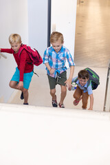 Caucasian elementary schoolboys with backpack climbing on steps in school building
