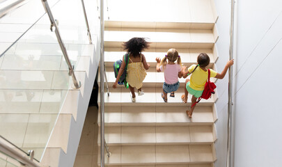 High angle view of multiracial elementary schoolgirls climbing steps in school building