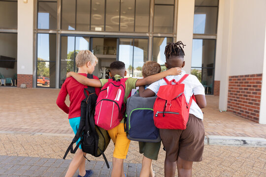 Rear view of multiracial elementary schoolboys with backpack and arm around standing campus