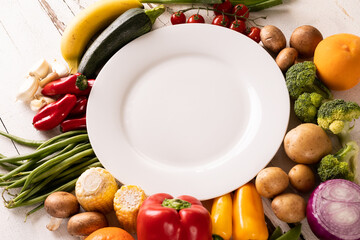 High angle view of empty white plate amidst various vegetables and fruits on table