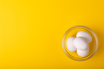 Directly above view of fresh white eggs in glass bowl by copy space on yellow background