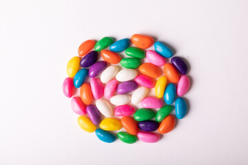 Overhead view of multi colored candies arranged in circle over white background with copy space