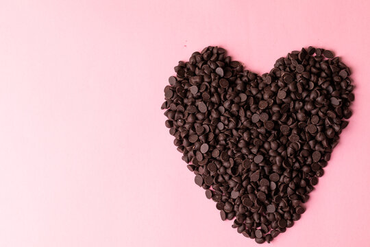 Directly above view of chocolate chips arranged as heart shape over pink background with copy space - Powered by Adobe