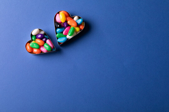 Directly above view of heart shape containers with colorful candies by copy space on blue background