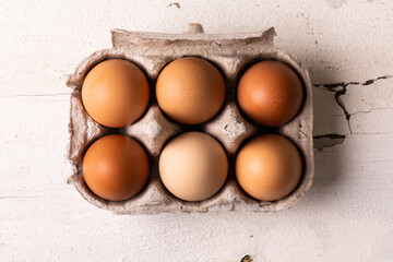 Directly above view of fresh brown eggs arranged in carton white wooden table