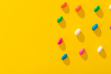 Directly above view of multi colored candies arranged by copy space on yellow background
