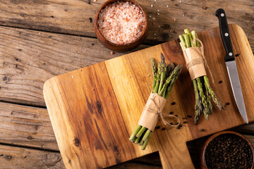 Directly above view of asparagus bunches by knife on wooden cutting board with rock salt on table