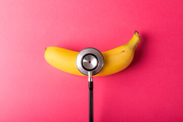 Directly above view of fresh banana with stethoscope by copy space over pink background - Powered by Adobe