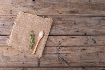 Directly above shot of rock salt in wooden spoon and rosemary on jute fabric at table