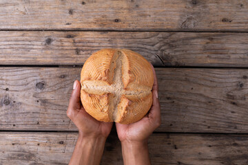 Cropped hands of african american man holding cross bun over wooden table