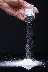 Cropped hand of african american man sprinkling salt with shaker against black background copy space