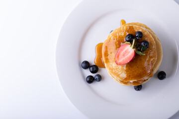 Directly above shot of stacked pancakes with syrup and berry fruits in plate on white background