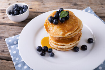 Close-up of blue berries and syrup on stacked pancakes in plate at table