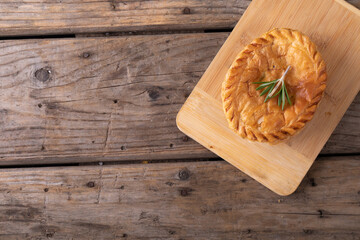 Directly above shot of baked stuffed pie with rosemary on wooden serving board at table