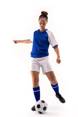 Full length of biracial young female soccer player kicking soccer ball against white background