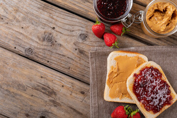 Overhead view of open face peanut butter and jelly sandwich on napkin with jars and strawberries