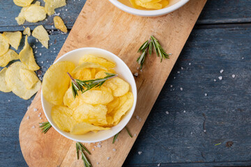 Close-up of potato chips in bowl with rosemary on serving board at wooden table