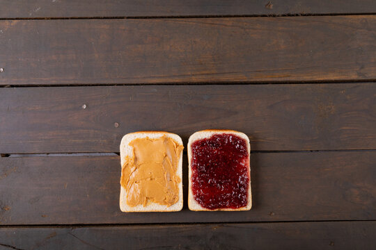 Overhead view of bread slices with peanut butter and preserves on wooden table