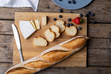 Overhead view of sliced baguette with blueberries, strawberry, cheese and knife on serving board