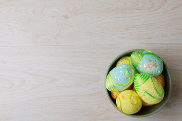 Overhead view of decorated easter eggs in bowl on table with empty space