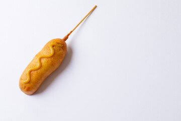 Close-up of corn dog with mustered sauce over skewer on white background with copy space