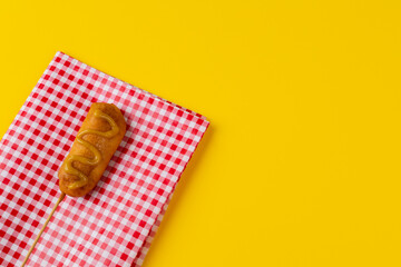 Corn dog with mustard sauce on checked pattern napkin over yellow background with copy space