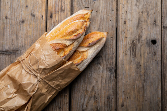 Overhead Close-up Of Baguettes Tied In Paper Bag On Wooden Table