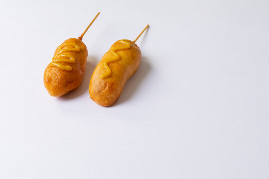 Close-up of corn dogs over skewers with mustard sauce on white background with copy space