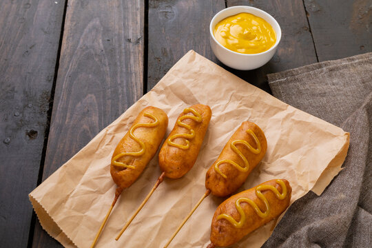 Close-up of mustered sauce on corn dogs over paper bag at wooden table