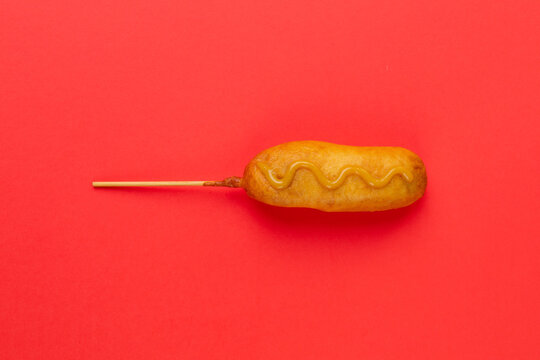 Overhead View Of Corn Dog With Mustered Sauce Over Skewer On Red Background With Copy Space