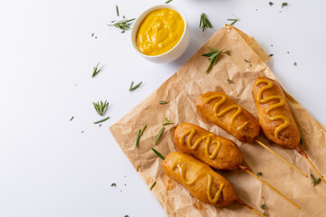 Corn dogs with mustered sauce and rosemary on paper bag on white background
