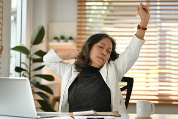 Satisfied middle aged woman stretching her body, resting at workplace enjoying break from work