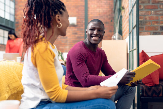 African american young male and female colleagues discussing over document while sitting on couch