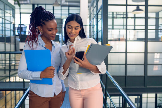 Smiling biracial young businesswoman showing smart phone to african american young female colleague