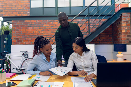 African american young businessman showing bar graph data to multiracial young female colleagues