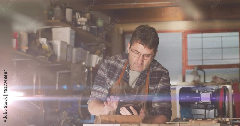 Poster animation of glowing light over caucasian man using tablet in workshop