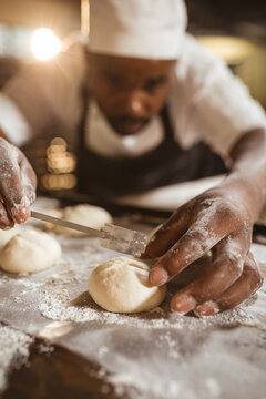Close-up of african american mid adult male baker making cross with blade on dough