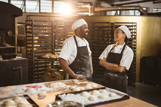 Smiling mid adult multiracial male and female bakers talking while standing in bakery