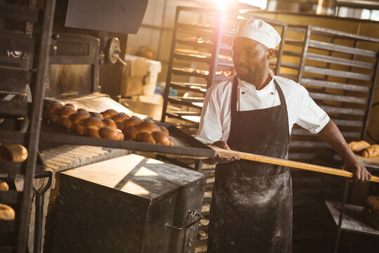 African american mid adult male baker keeping braided bread tray with long spatula in rack