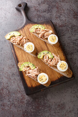 Rye Toast with canned tuna, boiled egg, ripe avocado and sesame seeds close-up on a wooden board on the table. Vertical top view from above