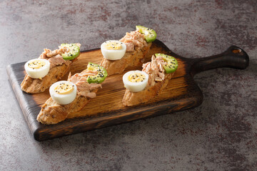 Obraz na płótnie Canvas Healthy eating toasts with tuna, avocado and egg, with sesame seeds and olive oil closeup on the wooden tray on the table. Horizontal