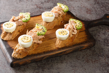 Obraz na płótnie Canvas Healthy diet sandwiches with canned tuna, boiled egg, ripe avocado and sesame close-up on a wooden board on the table. Horizontal