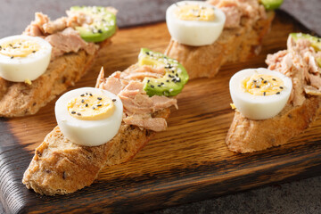Open sandwiches with canned tuna, boiled egg, ripe avocado and sesame seeds close-up on a wooden board on the table. Horizontal