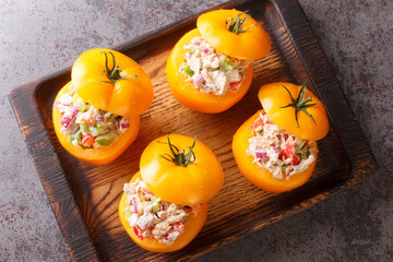 Tomatoes stuffed with a salad of canned tuna, bell peppers, onions and greens close-up on a wooden tray on the table. Horizontal top view from above