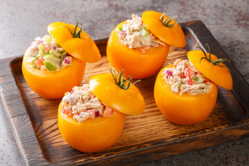 Tomatoes stuffed with a salad of canned tuna, bell peppers, onions and greens close-up on a wooden tray on the table. Horizontal
