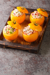 Fresh yellow tomatoes stuffed with tuna salad and vegetables close-up on a wooden tray on the table. Vertical