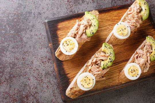 Open sandwiches with canned tuna, boiled egg, ripe avocado and sesame seeds close-up on a wooden board on the table. Horizontal top view from above
