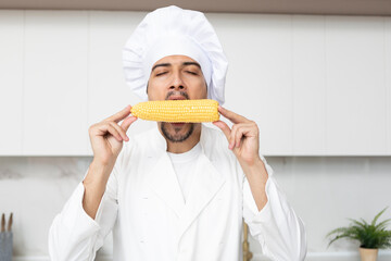 Close up portrait of handsome male chef eating maize in the kitchen