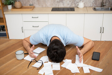 Close up of shocked man sitting at the table, stressed and confused by calculate expense from...
