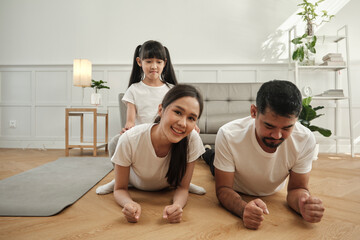 Happy well-being Asian Thai family, children play and tease their parents while yoga fitness training and health exercise together in the white living room, domestic home lifestyle, weekend activity.